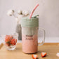 Mason Juicer with pink smoothie and straw on a wooden surface with strawberries.